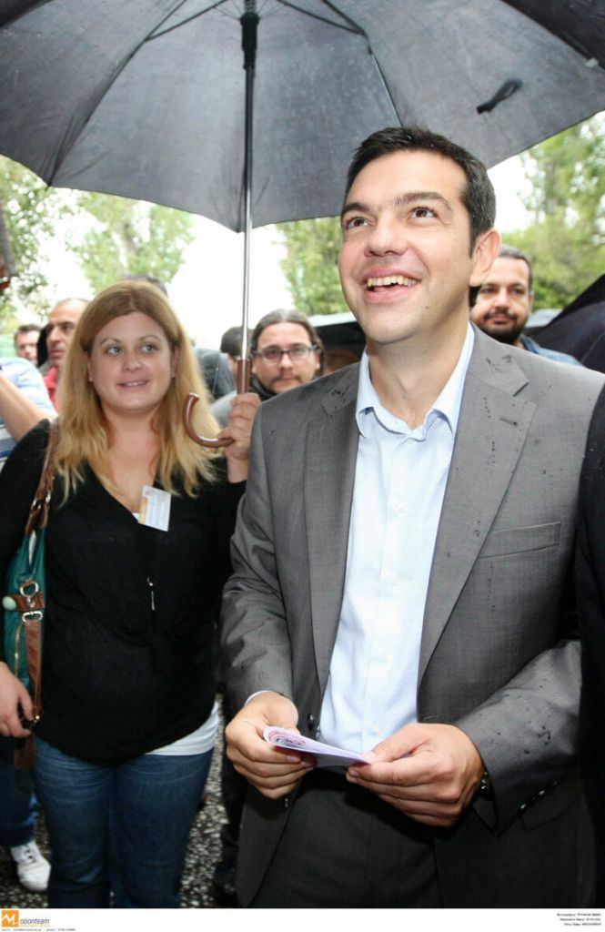 Η υφυπουργός Ελευθερία Χατζηγεωργίου κρατώντας την ομπρέλα του Τσίπρα